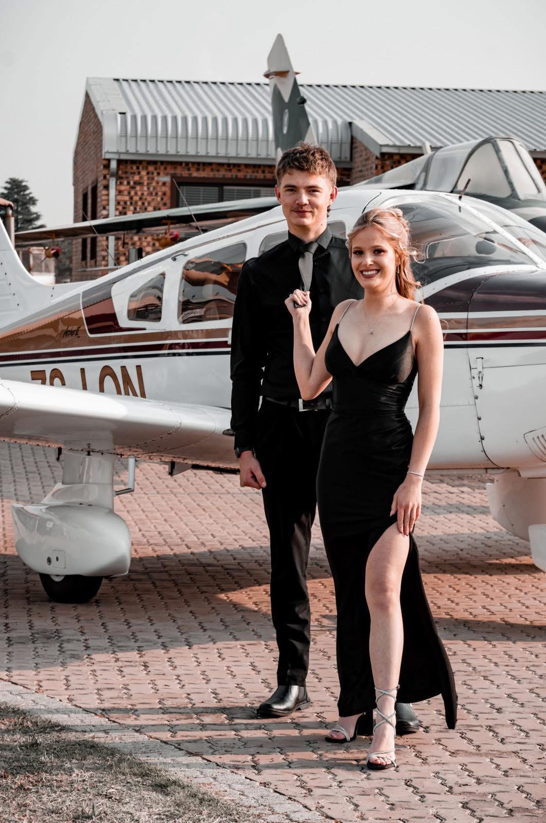 Matric farewell couple dressed in black beside an airplane