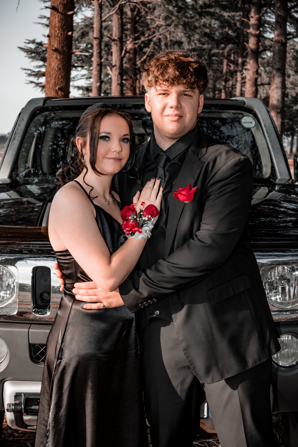 Matric farewell couple in a black satin dress with red roses beside a car